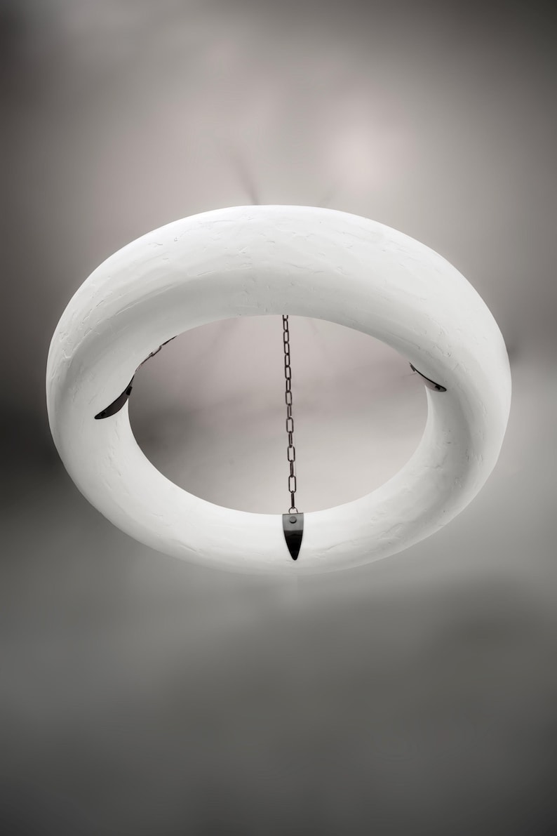 May include: A white circular pendant light fixture with a chain hanging from the center. The fixture is made of a textured material and has a simple, modern design.
