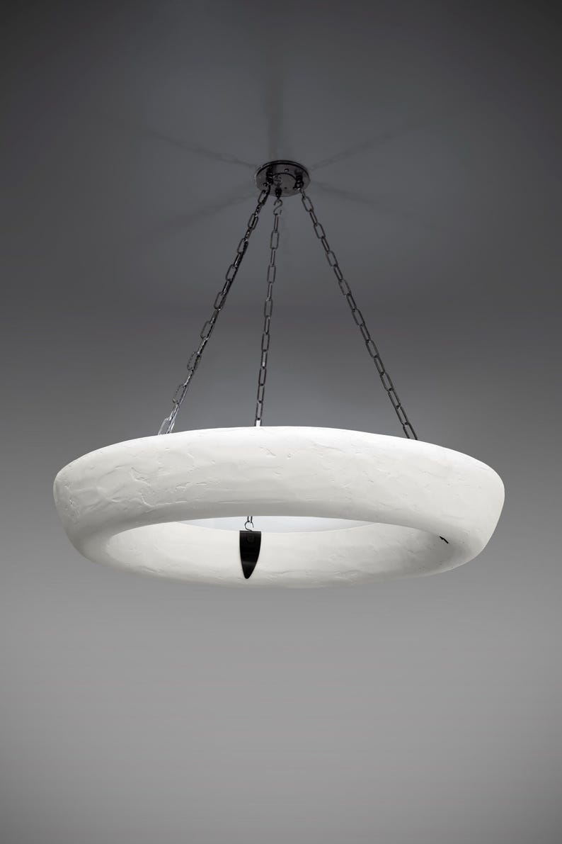 May include: A white circular pendant light fixture hangs from a chain. The fixture is made of a textured material and has a hole in the center.