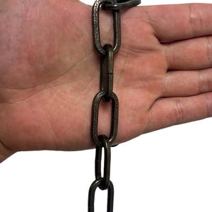 Puede incluir: Cadena de color bronce oscuro con eslabones texturizados. La cadena es de metal y tiene un diseño de eslabón ovalado. La cadena se muestra sobre un fondo blanco.