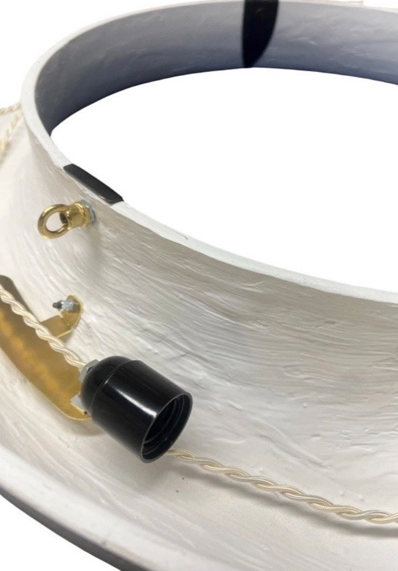 May include: White ceiling fixture with a black electrical socket and a gold metal bracket. The fixture has a white cord with a braided texture.