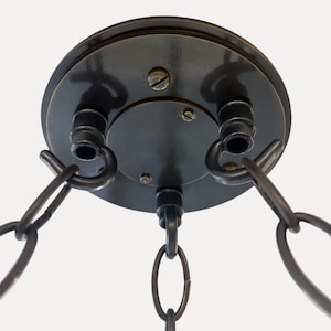 May include: A black metal ceiling fixture with three chains hanging down. The fixture has a round base with two hooks on the side.