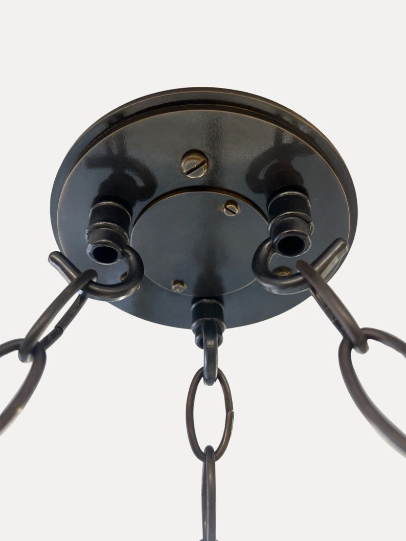 May include: A black metal ceiling fixture with three chains hanging down. The fixture has a round base with two hooks on the side.