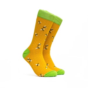 May include: A pair of yellow socks with a honeycomb pattern and small bee illustrations. The socks have green tops.