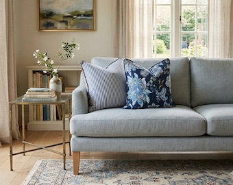 May include: A light gray sofa featuring two decorative throw pillows. One pillow has a navy blue and white vertical stripe pattern, while the other displays a dark blue floral print with white and light blue petals on a deep blue background.