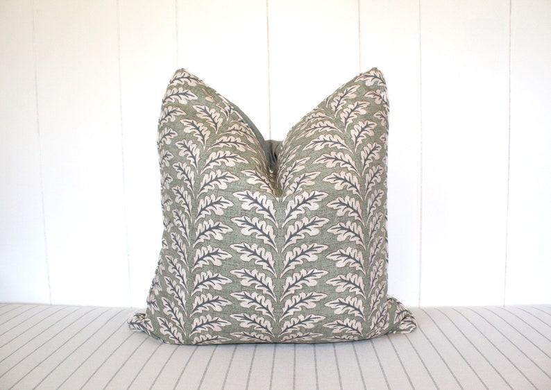 Puede incluir: Una almohada de tiro verde y blanca con un dise&ntilde;o de hojas. La almohada est&aacute; hecha de una tela suave y texturizada.