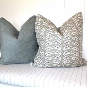 Puede incluir: Dos almohadas decorativas en un banco a rayas. Una almohada es de color verde azulado s&oacute;lido y la otra es una almohada verde estampada con un dise&ntilde;o de hojas blancas.