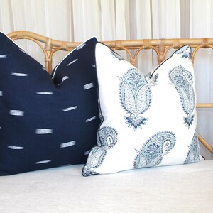 May include: Two decorative throw pillows on a light-colored wicker couch. One pillow is navy blue with white stripes, and the other is white with a blue paisley pattern.