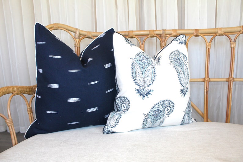 May include: Two decorative throw pillows on a light-colored wicker couch. One pillow is navy blue with white stripes, and the other is white with a blue paisley pattern.