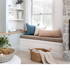 K&ouml;nnte beinhalten: Ein Fensterplatz mit einem braunen Kissen und zwei Dekokissen, eines blau und eines beige. Ein geflochtener Korb mit einer wei&szlig;en Decke steht auf dem Boden vor dem Fensterplatz. Das Fenster hat einen braunen Rollladen. Der Text "Our cushions had been featured in Home Beautiful Magazine March 2022" ist am unteren Rand des Bildes zu sehen.