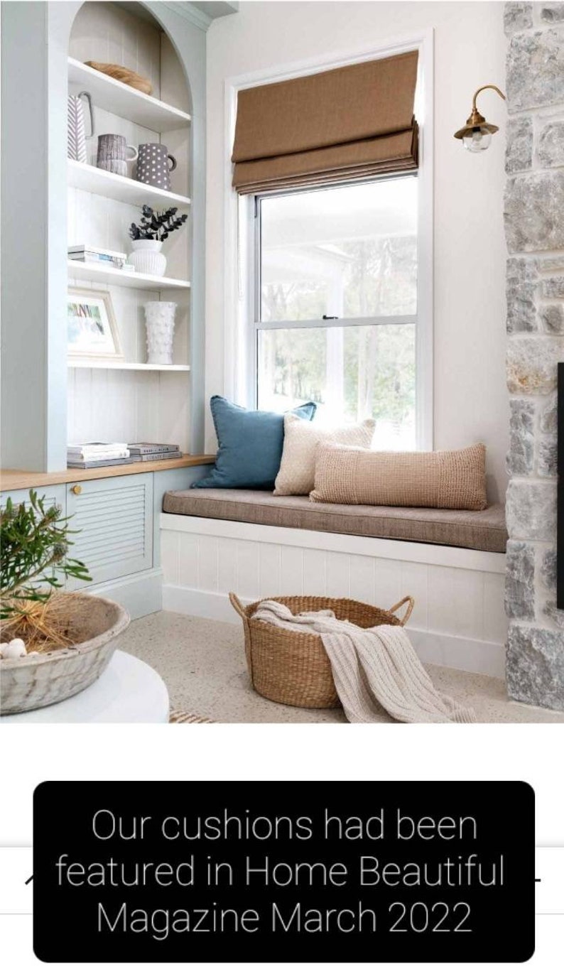 K&ouml;nnte beinhalten: Ein Fensterplatz mit einem braunen Kissen und zwei Dekokissen, eines blau und eines beige. Ein geflochtener Korb mit einer wei&szlig;en Decke steht auf dem Boden vor dem Fensterplatz. Das Fenster hat einen braunen Rollladen. Der Text "Our cushions had been featured in Home Beautiful Magazine March 2022" ist am unteren Rand des Bildes zu sehen.