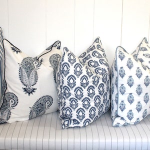 May include: Five decorative throw pillows with blue and white patterns. The pillows are arranged in a row on a white striped surface.