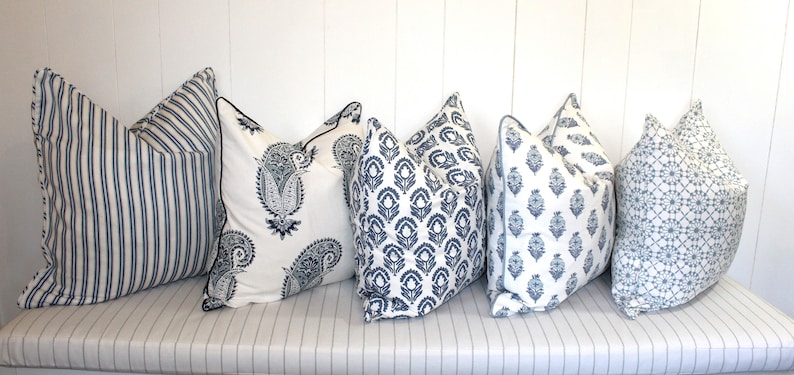 May include: Five decorative throw pillows with blue and white patterns. The pillows are arranged in a row on a white striped surface.