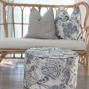 K&ouml;nnte beinhalten: Ein wei&szlig;es Weiden-Sofa mit einem wei&szlig;en Kissen und zwei blauen und wei&szlig;en Kissen mit Mustern. Vor dem Sofa steht ein runder blauer und wei&szlig;er Hocker.