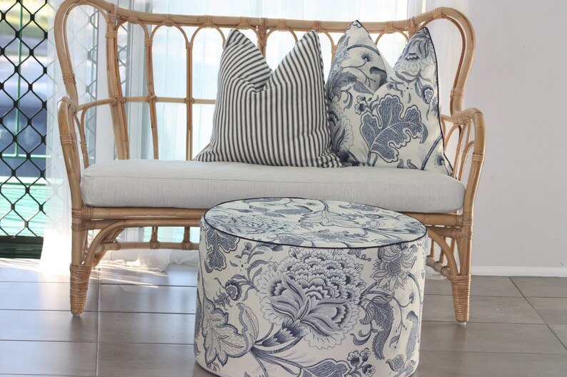 K&ouml;nnte beinhalten: Ein wei&szlig;es Weiden-Sofa mit einem wei&szlig;en Kissen und zwei blauen und wei&szlig;en Kissen mit Mustern. Vor dem Sofa steht ein runder blauer und wei&szlig;er Hocker.