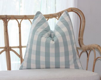 May include: A light blue and white checkered throw pillow on a wicker sofa.