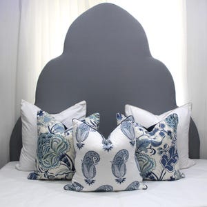 May include: A gray headboard with a unique arched shape, decorated with four throw pillows. Two pillows feature a white background with blue and green floral patterns, while the other two pillows have a white background with blue paisley patterns.