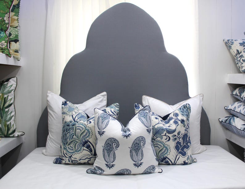 May include: A gray headboard with a unique arched shape, decorated with four throw pillows. Two pillows feature a white background with blue and green floral patterns, while the other two pillows have a white background with blue paisley patterns.