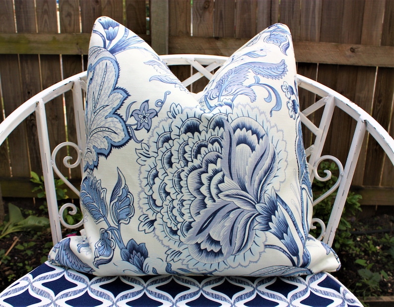 K&ouml;nnte beinhalten: Ein wei&szlig;es Kissen mit einem blauen und wei&szlig;en Blumenmuster. Das Kissen liegt auf einem wei&szlig;en Metallstuhl mit einem blauen und wei&szlig;en gemusterten Sitz.
