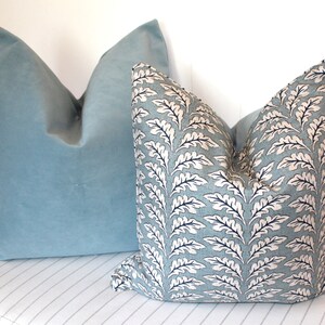 Puede incluir: Dos almohadas decorativas, una es de terciopelo azul claro liso y la otra es una almohada azul claro estampada con un dise&ntilde;o de hojas blancas y negras.