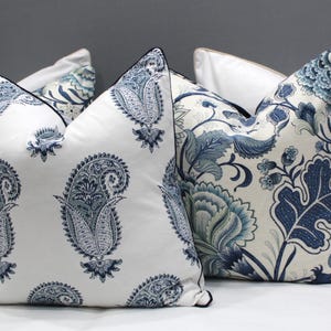 May include: Four decorative throw pillows with a white background and blue floral patterns. The pillows are arranged on a gray bed.