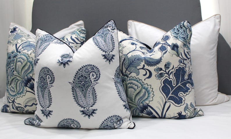 May include: Four decorative throw pillows with a white background and blue floral patterns. The pillows are arranged on a gray bed.