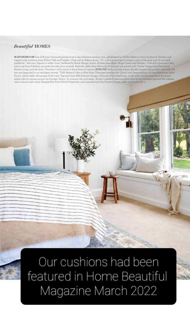 K&ouml;nnte beinhalten: Ein wei&szlig;es Schlafzimmer mit einer gro&szlig;en Fensterbank, einem Bett mit einer gestreiften Bettdecke und einem Holzhocker. Die Fensterbank ist mit einem elfenbeinfarbenen Stoff bezogen und hat eine Wolldecke. Der Text "Our cushions had been featured in Home Beautiful Magazine March 2022" befindet sich am unteren Rand des Bildes.