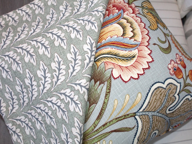 Puede incluir: Dos almohadas decorativas con patrones florales. Una almohada tiene un fondo verde claro con dise&ntilde;os de hojas blancas. La otra almohada tiene un fondo azul claro con un dise&ntilde;o floral colorido.