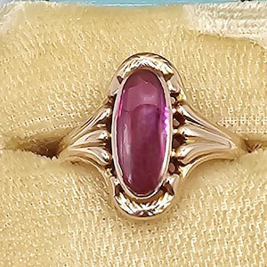 May include: A gold ring with a large oval-shaped pink gemstone set in a gold bezel. The ring is in a velvet ring box.