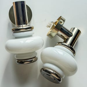 May include: Two vintage wall sconces with a white, rounded glass body and chrome accents. The sconces have a cylindrical chrome stem and a circular chrome base. One sconce has a detached electrical component.