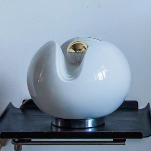 Può includere: Una lampada da tavolo in ceramica bianca con una lampadina dorata e una base in metallo nero. La lampada è appoggiata su un vassoio in metallo nero.