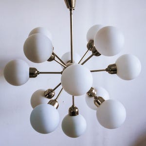 May include: A brass and white glass chandelier with 10 light bulbs. The chandelier has a starburst design with the light bulbs arranged in a circle around a central point.