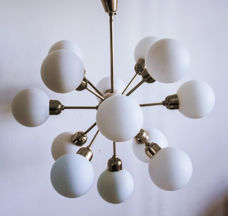 May include: A brass and white glass chandelier with 10 light bulbs. The chandelier has a starburst design with the light bulbs arranged in a circle around a central point.