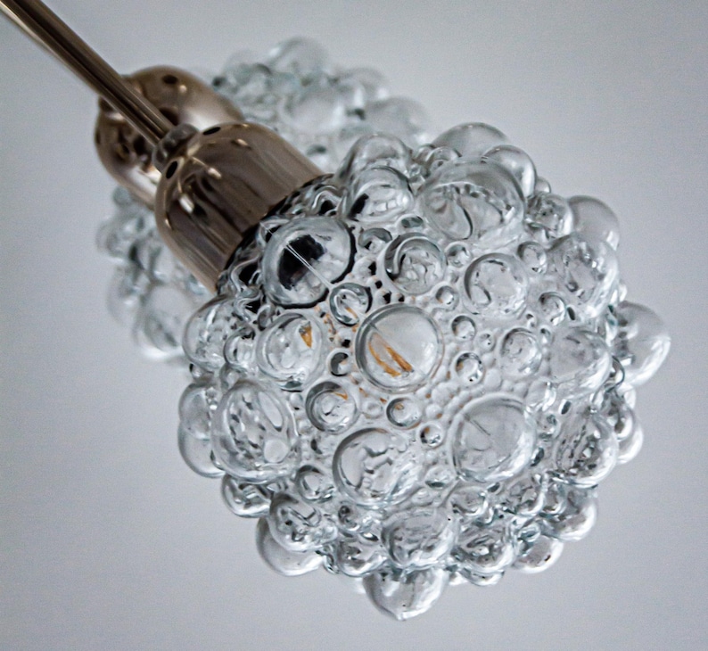 May include: Close-up of a clear glass pendant light fixture with a bubbled texture. The light fixture is attached to a silver metal rod.