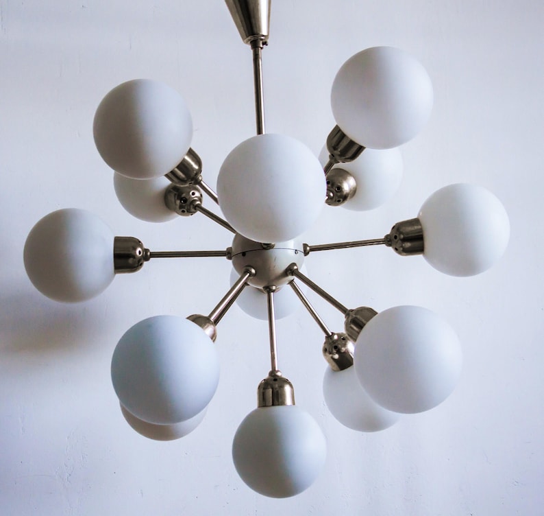May include: A modern, mid-century style chandelier with a brass finish and ten white frosted glass globes. The chandelier has a starburst design with the globes extending outward from a central point.