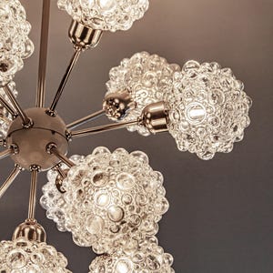 May include: A chrome and glass chandelier with six bubble-shaped light fixtures. The chandelier has a modern design and is perfect for a mid-century modern home.