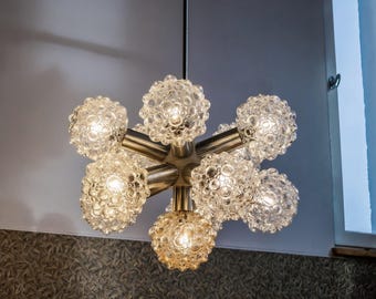 Puede incluir: Una lámpara de araña de plata y vidrio con seis bombillas. La lámpara de araña tiene un diseño de estrella con seis brazos, cada uno terminando en un globo de vidrio transparente con una superficie texturizada. Los globos están iluminados por las bombillas, creando un brillo cálido.