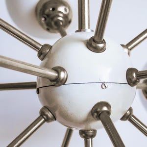 May include: A white globe chandelier with multiple silver metal arms extending outwards. The globe has a smooth, slightly textured surface.