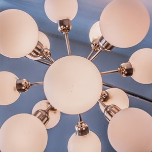 May include: A modern, white, frosted glass chandelier with a silver metal frame. The chandelier has eight light bulbs and a starburst design.
