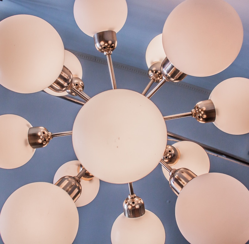 May include: A modern, white, frosted glass chandelier with a silver metal frame. The chandelier has eight light bulbs and a starburst design.