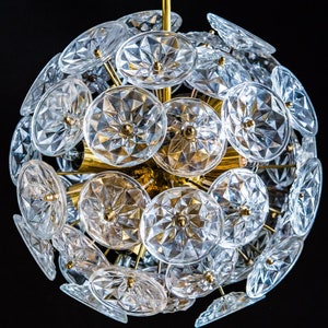 Op de afbeelding: Een gouden kroonluchter met een bolvorm, versierd met talloze heldere glazen kristallen. De kroonluchter heeft een modern ontwerp en is perfect om elke kamer een vleugje elegantie te geven.