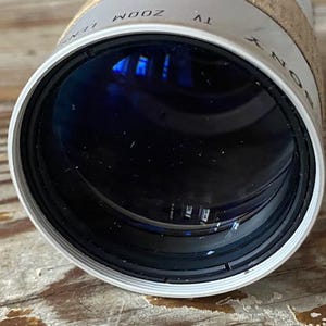 K&ouml;nnte beinhalten: Nahaufnahme eines Sony TV-Zoomobjektivs. Das Objektiv ist zylindrisch mit einem wei&szlig;en und schwarzen Rand. Das Objektiv hat ein dunkles Inneres mit Reflexionen. Die W&ouml;rter "SONY" und "TV ZOOM" sind auf dem Objektiv sichtbar.