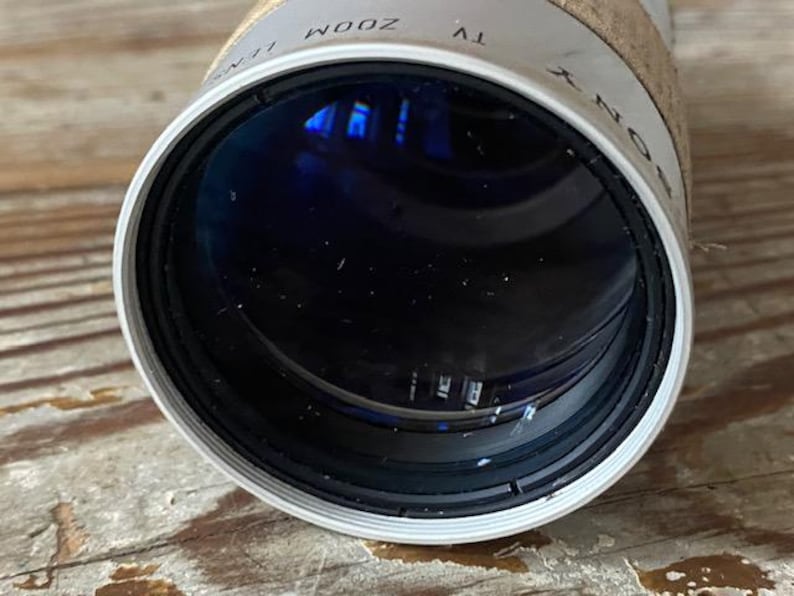 K&ouml;nnte beinhalten: Nahaufnahme eines Sony TV-Zoomobjektivs. Das Objektiv ist zylindrisch mit einem wei&szlig;en und schwarzen Rand. Das Objektiv hat ein dunkles Inneres mit Reflexionen. Die W&ouml;rter "SONY" und "TV ZOOM" sind auf dem Objektiv sichtbar.