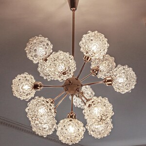 May include: A brass and glass chandelier with eight clear glass globe shades. The shades have a textured bubbled surface. The chandelier has a long, thin, brass chain.