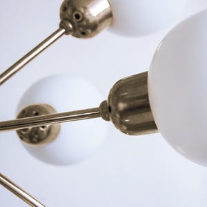 May include: A gold-toned ceiling light fixture with three white glass globes. The fixture has a modern design with sleek, straight lines.