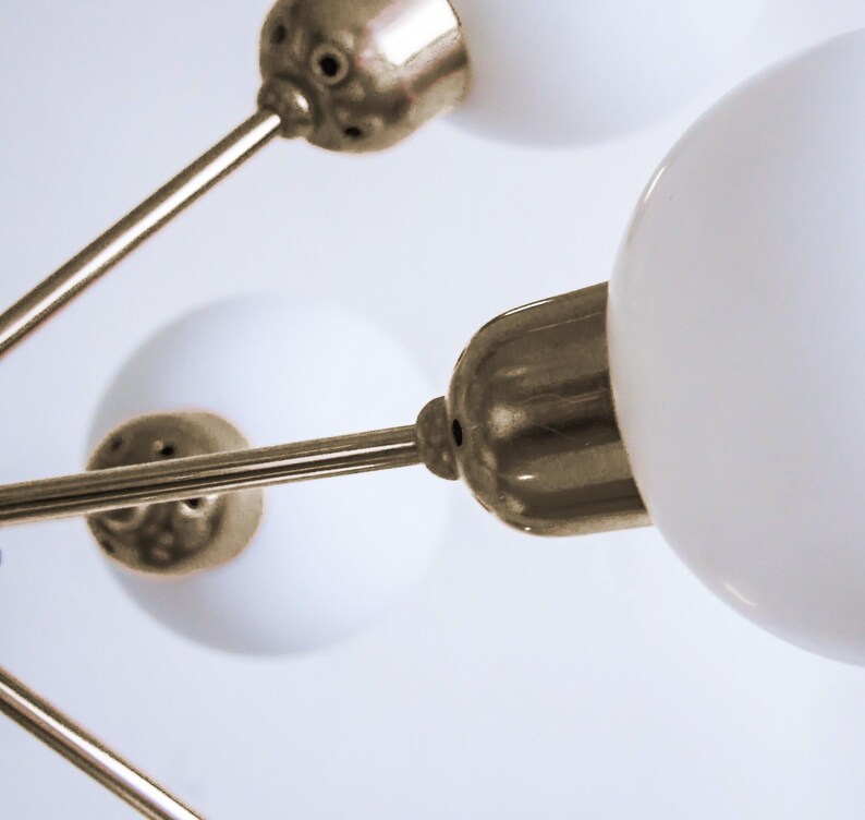May include: A gold-toned ceiling light fixture with three white glass globes. The fixture has a modern design with sleek, straight lines.