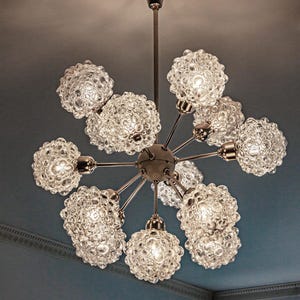 May include: A silver chandelier with 9 clear glass globe light fixtures. Each globe has a textured bubbled surface.