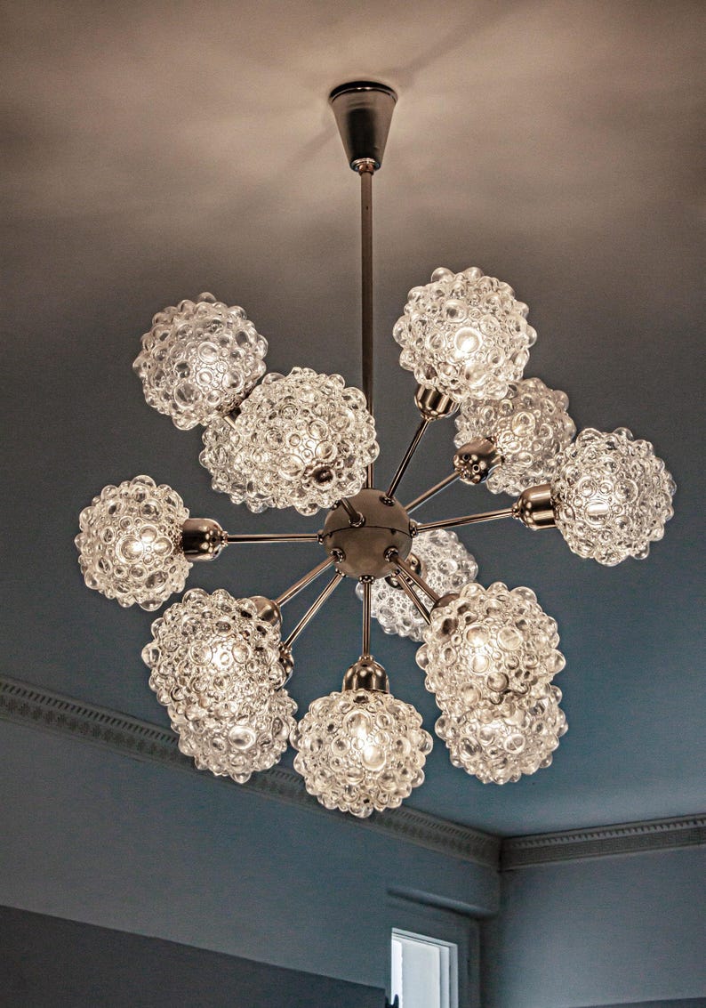 May include: A silver chandelier with 9 clear glass globe light fixtures. Each globe has a textured bubbled surface.