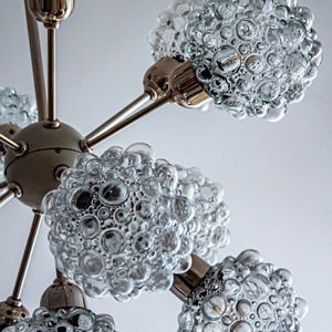 May include: A chrome and glass chandelier with six light fixtures. Each fixture has a clear glass shade with a bubbled texture.