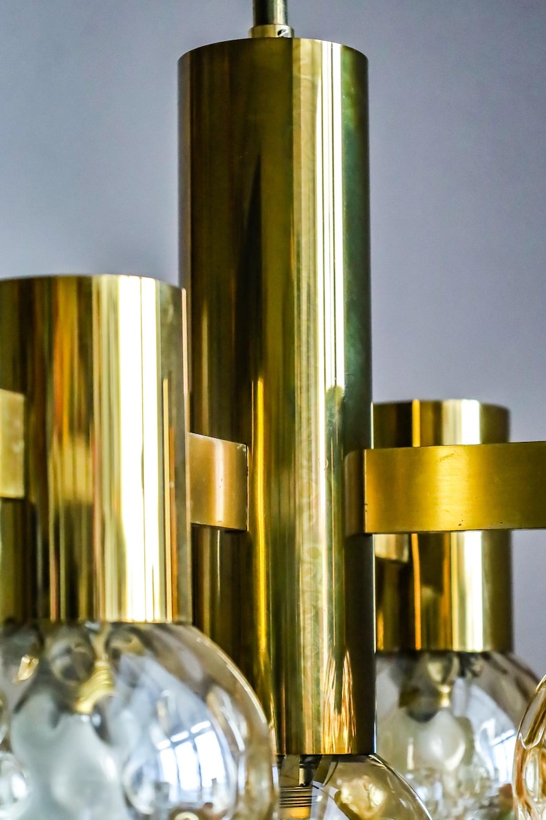 May include: A brass chandelier with multiple globe-shaped glass shades. The chandelier has a polished brass finish and a modern design.