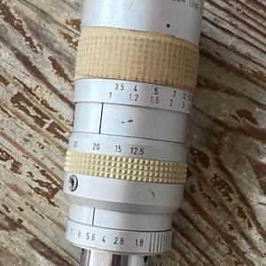 K&ouml;nnte beinhalten: Ein Vintage Sony TV Zoom-Objektiv mit silbernem Geh&auml;use und beigefarbenen und wei&szlig;en strukturierten Griffen. Das Objektiv hat verschiedene numerische Markierungen und eine schwarze Objektivkappe. Der Text "SONY TV ZOOM LENS" ist sichtbar.